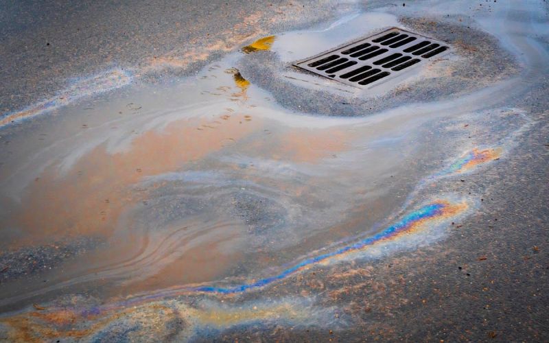 oil slick on road flowing into storm drain