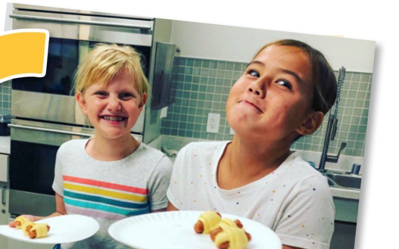 two children playfully smiling and holding reusable dishes with food on them