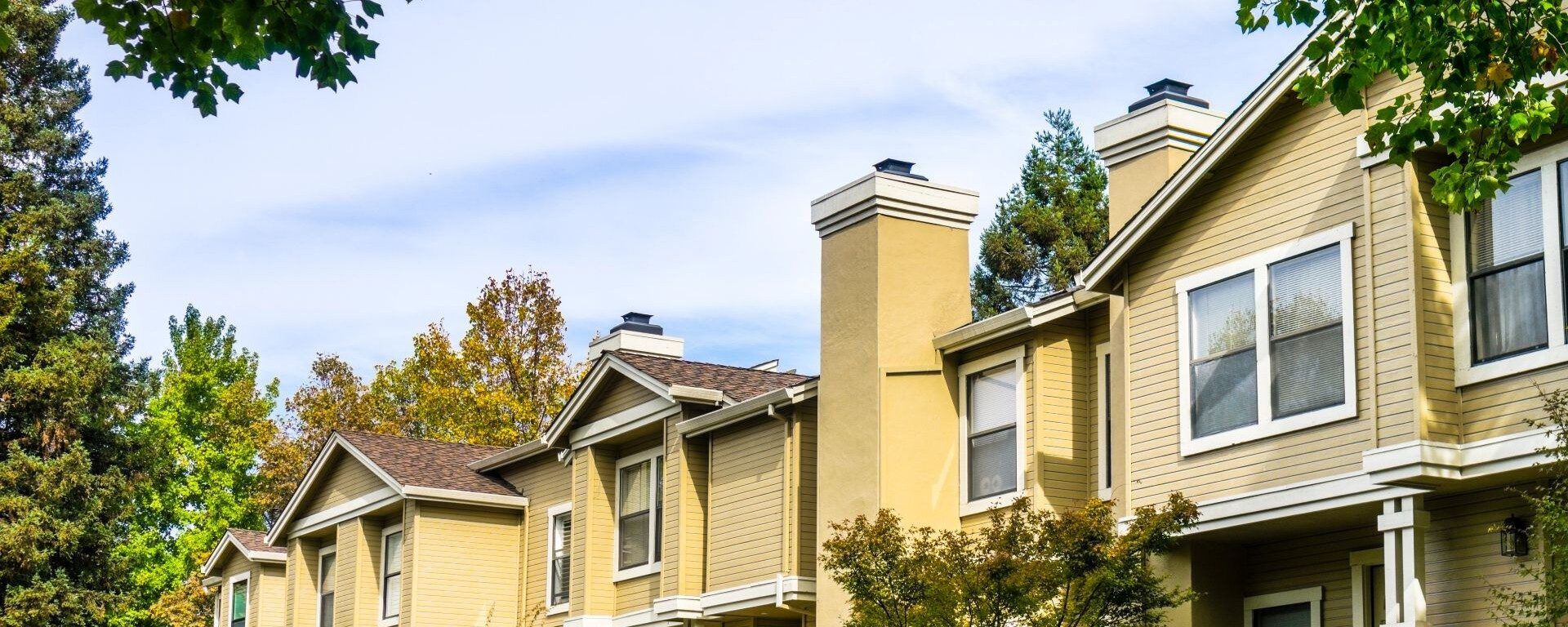 Row of yellow multi-family property homes and trees.