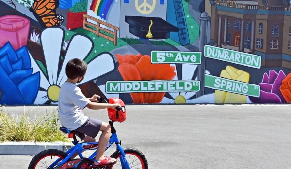 young boy rides bicycle past vibrant city mural