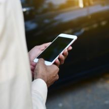 closeup of man using smart phone while standing beside a car