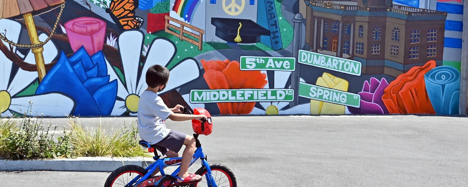 young boy rides bicycle past vibrant mural in North Fair Oaks neighborhood in San Mateo County