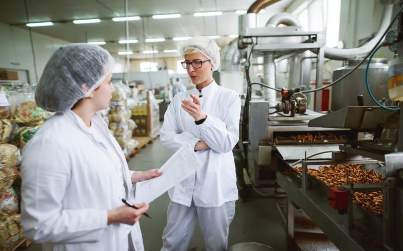 two women in hairnets discuss food safety in a commercial kitchen