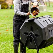person dumping food scraps from kitchen pail into backyard compost tumbler