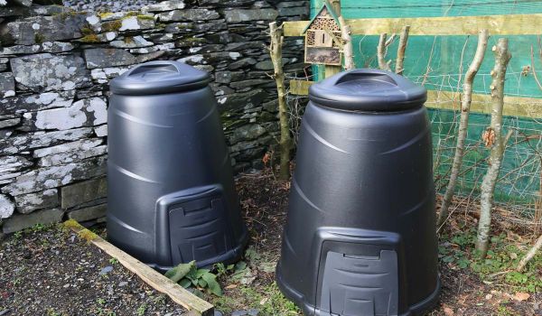 two home composting bins next to raised garden bed and mason bee house