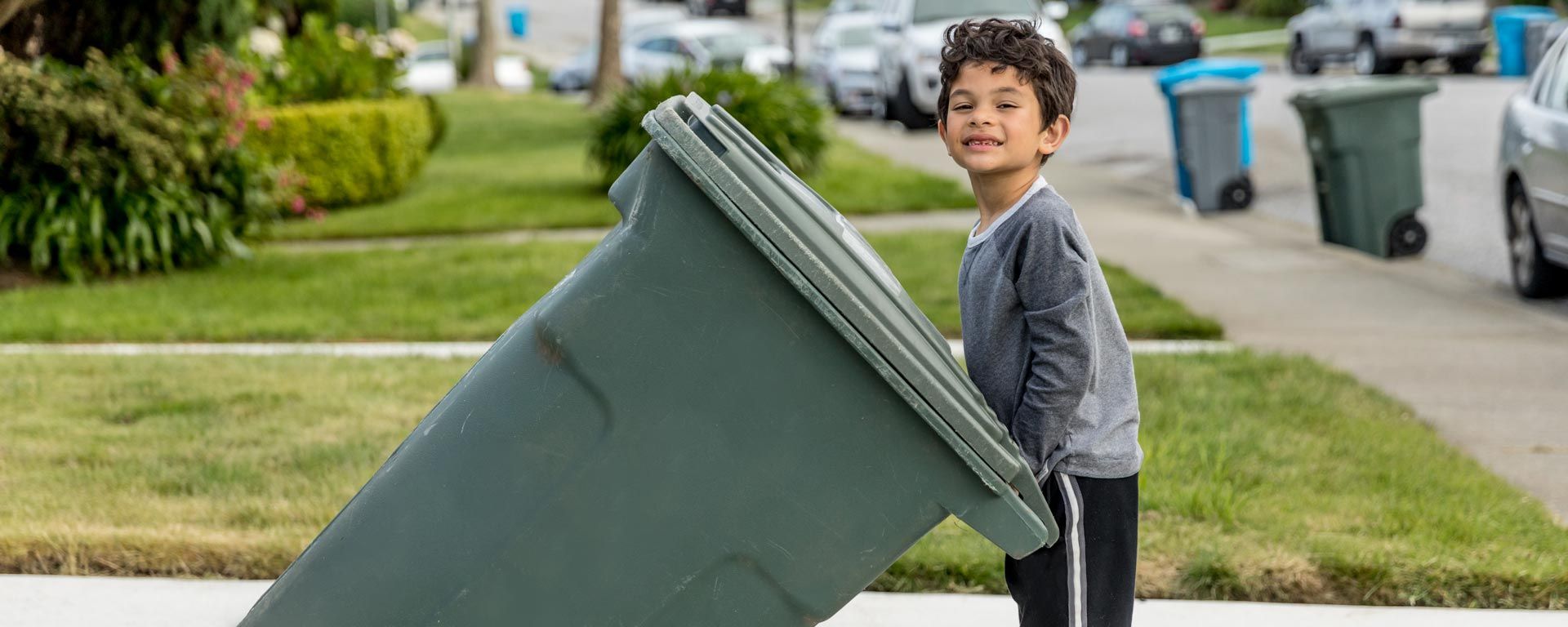 Child rolling in the green organics collection bin in a driveway outside of a home
