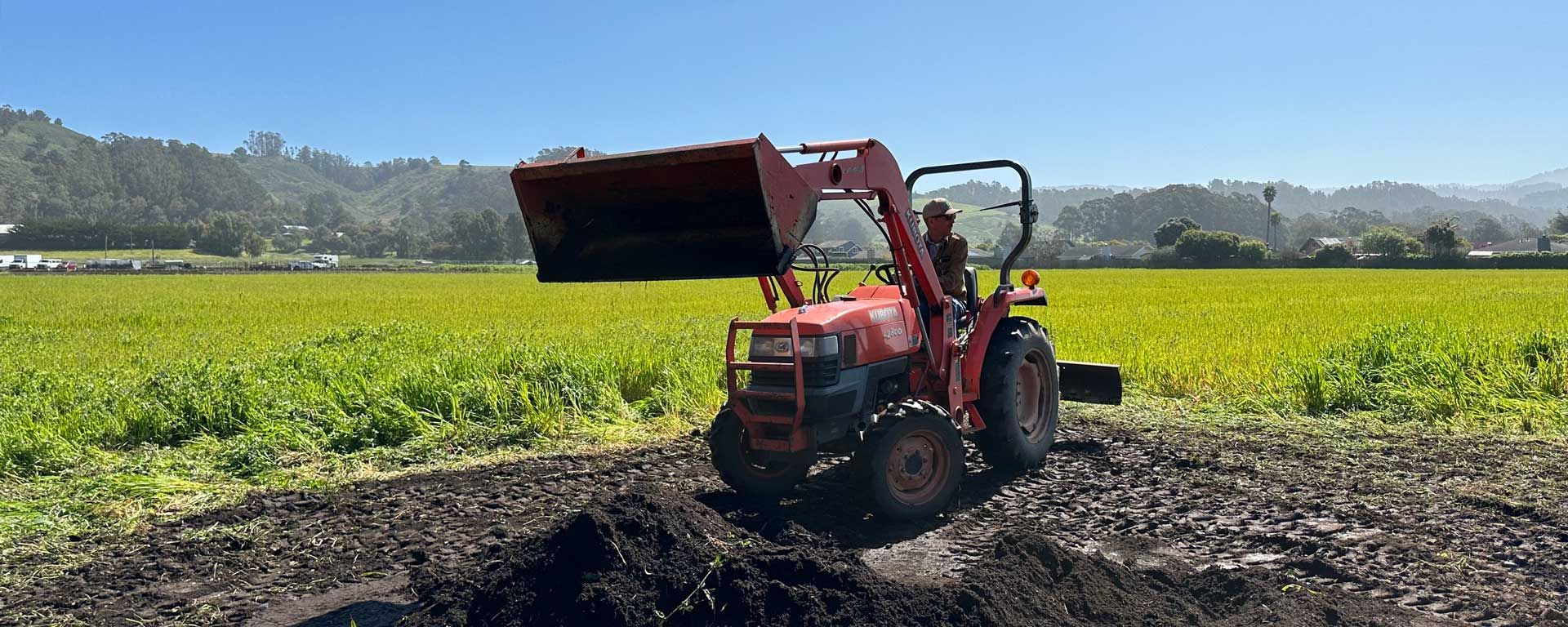 farmer spreading compost on field with tractor