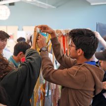 Youth Climate Ambassadors Leadership Program students work together in classroom on project attaching strips of fabric with writing on them to wooden frame