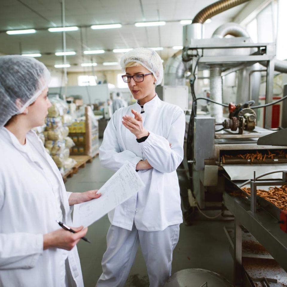 two women in hairnets discuss food safety in a commercial kitchen