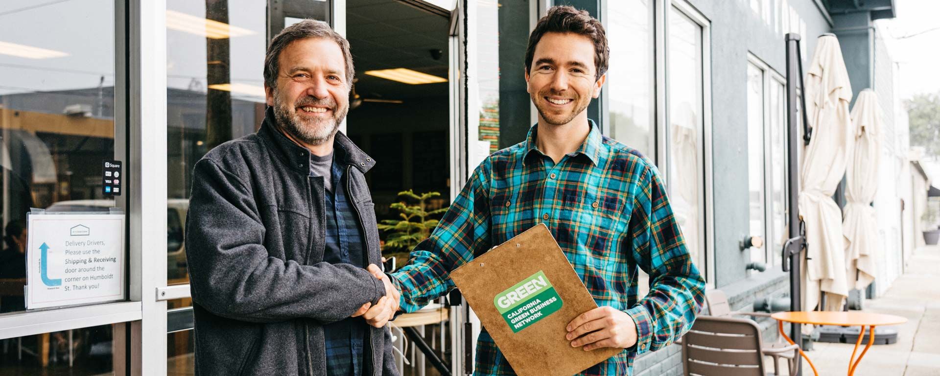 Sustainability Department staff shakes hand of business owner receiving green business certification award in front of his business