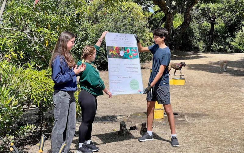 three Youth Climate Ambassador Leadership Program students in a local park display their Community Impact Project poster of native plants
