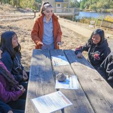 Sustainability Department educator talks with four middle school students at picnic table by a pond