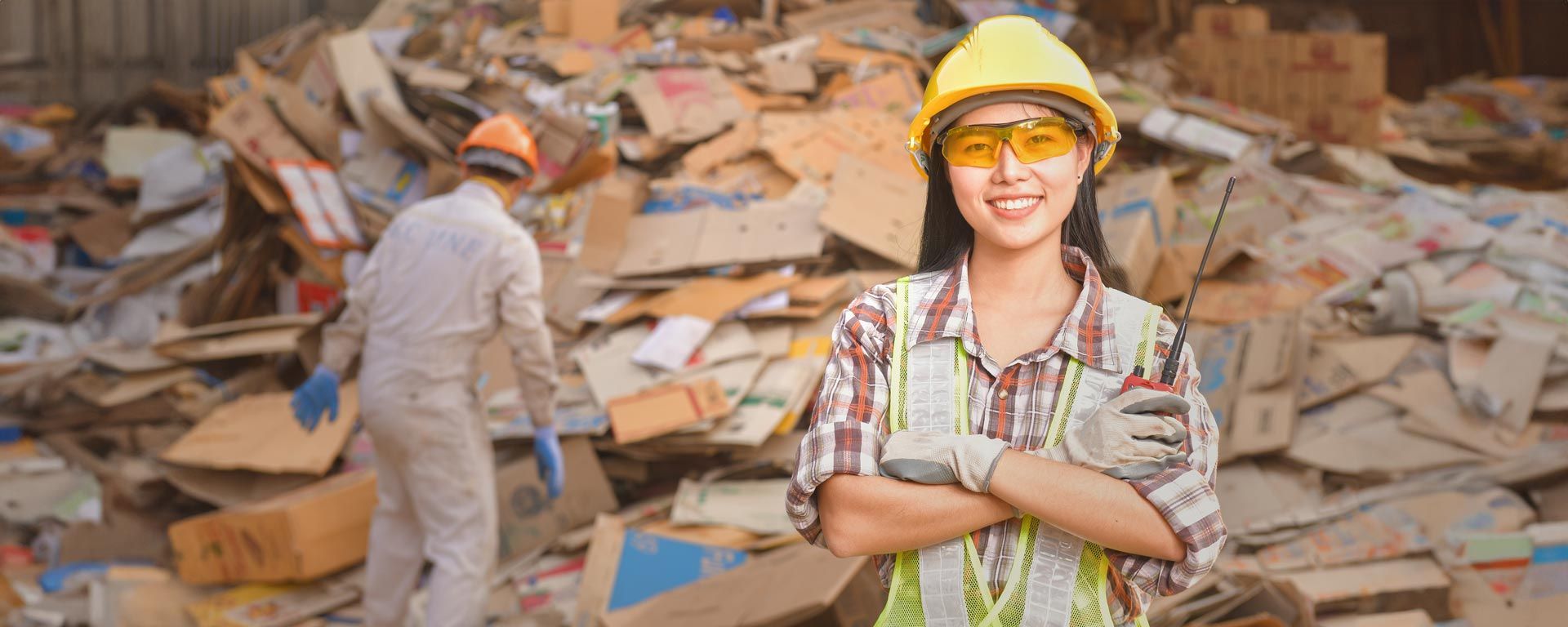 female recycling center employee stands in front of pile of cardboard for recycling