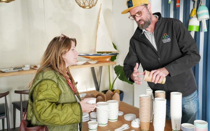 Sustainability Department staff member showing compostable disposable cups and foodware to woman small business owner