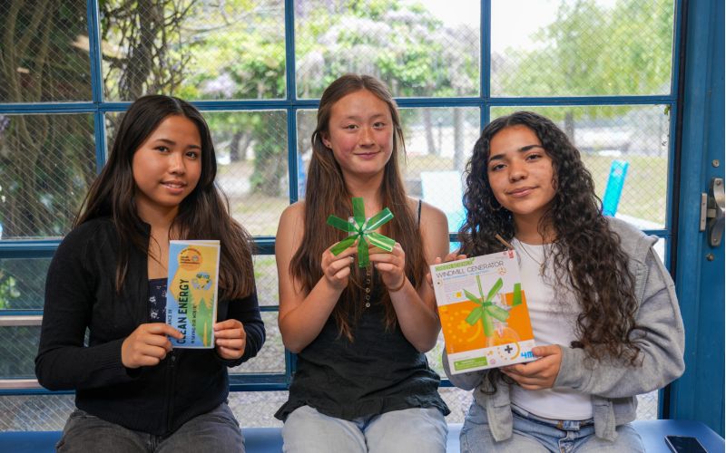 Three high school students hold educational materials about clean energy.