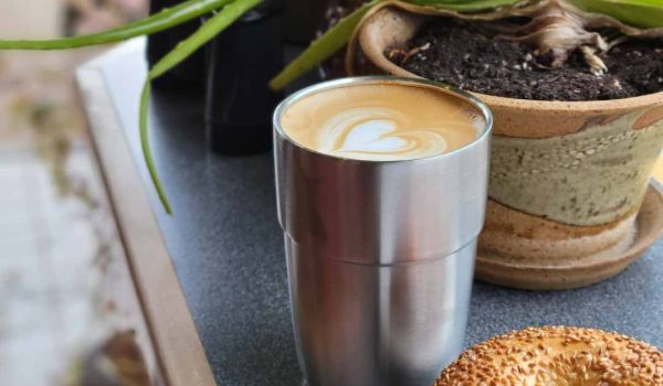 reusable stainless steel of coffee next to a plant and bagel in coffee shop