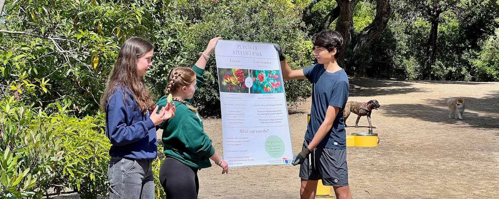 three students in Youth Climate Ambassadors program hold up their project poster in local park