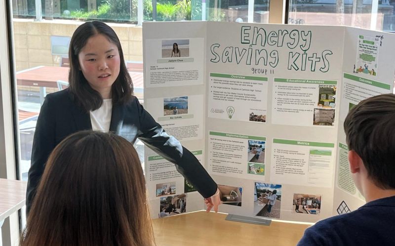 Youth Climate Ambassador Leadership Program student points towards her Community Impact Project poster titled Energy Saving Kits