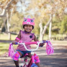 young girl riding bicycle and wearing pink helmet