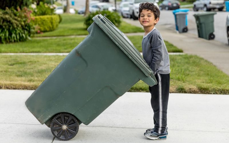 youth pushes curbside green waste bin outside of home