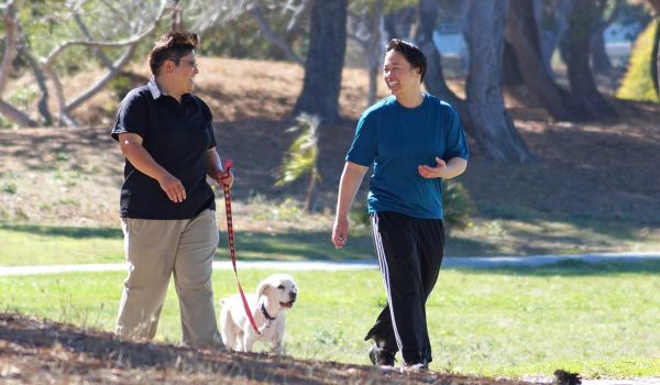 two people talking while walking a dog on leash in a park