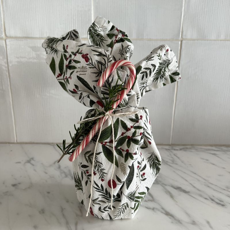 A festive dish towel wrapped around a gift with a candy cane attached to it.
