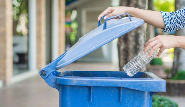 woman putting plastic water bottle in recycling bin
