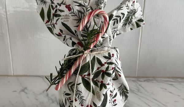 A festive dish towel wrapped around a gift with a candy cane attached to it.