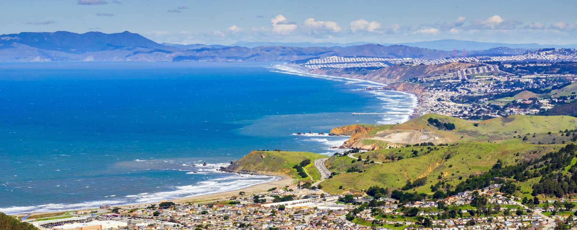 aerial view of San Mateo County coastline with ocean, cities and mountains beyond