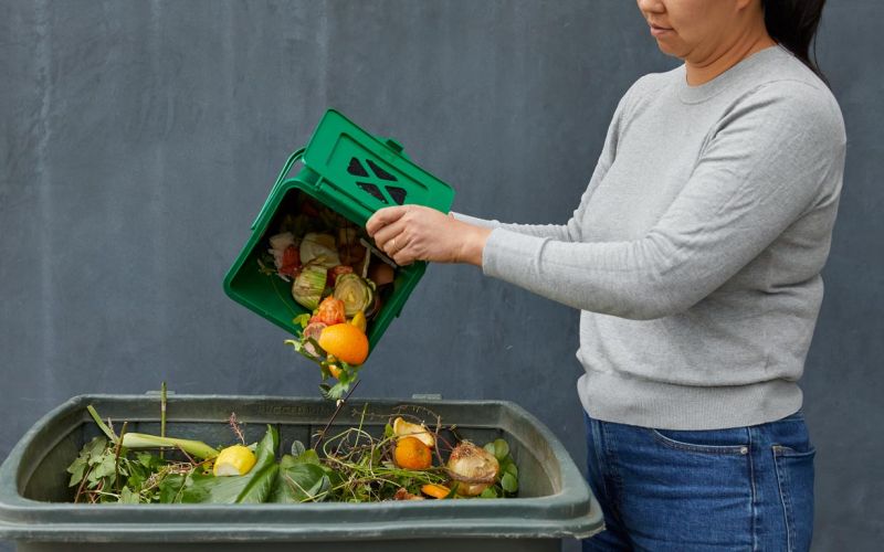 woman dumping food scraps into green waste bin