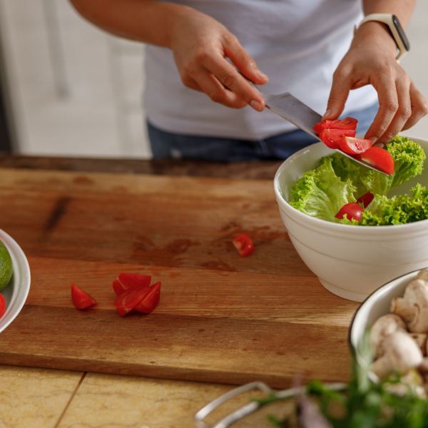 A person adds sliced tomatoes to a salad bowl on a cutting board