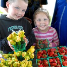 two children at farmers market holding baskets of strawberries and zucchini blossoms