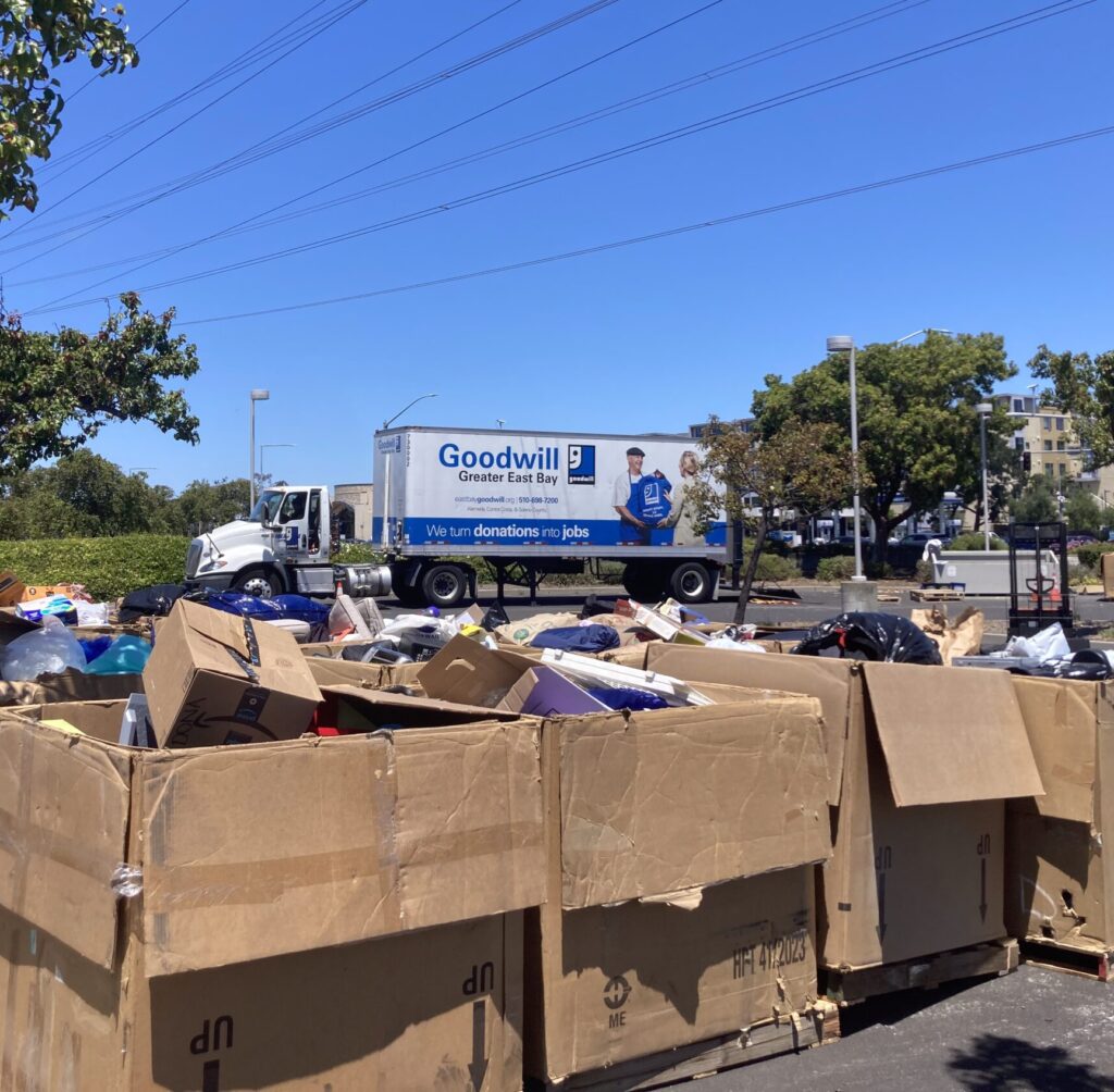 Three large cardboard boxes full of items in front of a Goodwill box truck. 
