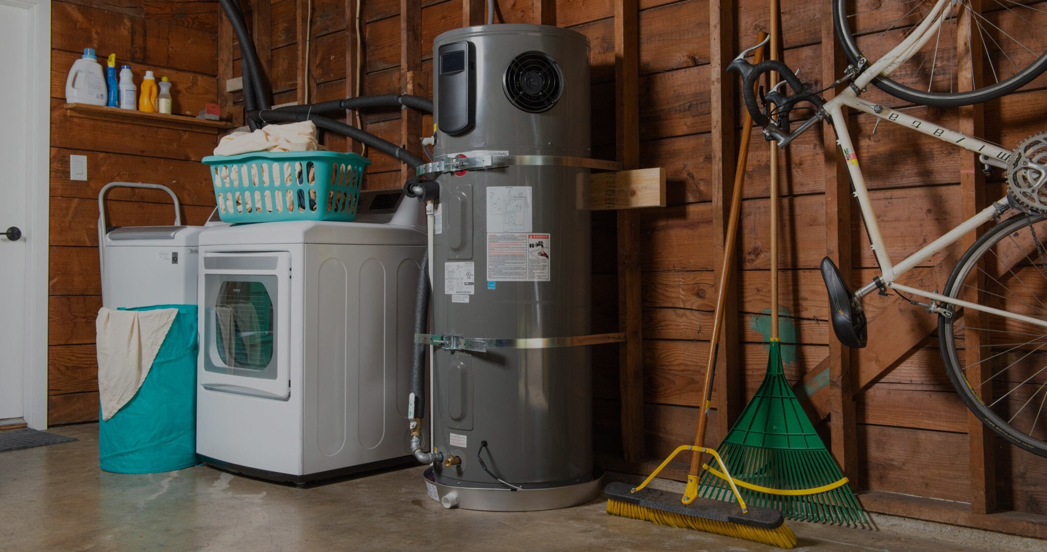 Gray heat pump water heater in a garage next to a washing machine.