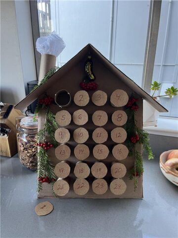 House shaped advent calendar made out of brown recycled paper. The house structure is sitting on a bright kitchen countertop. 