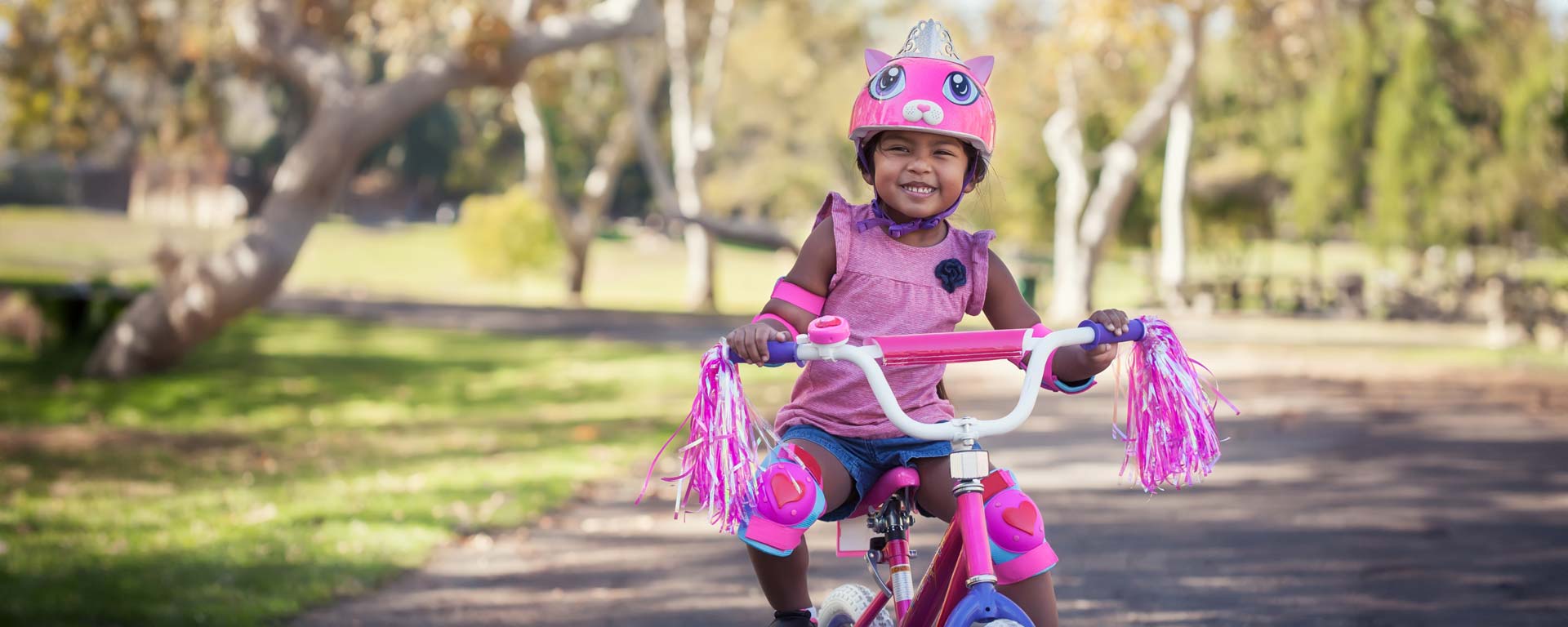 young girl riding bike and wearing a pink helmet