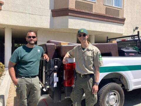 Two park rangers posing in front of a truck full of Surplus items.
