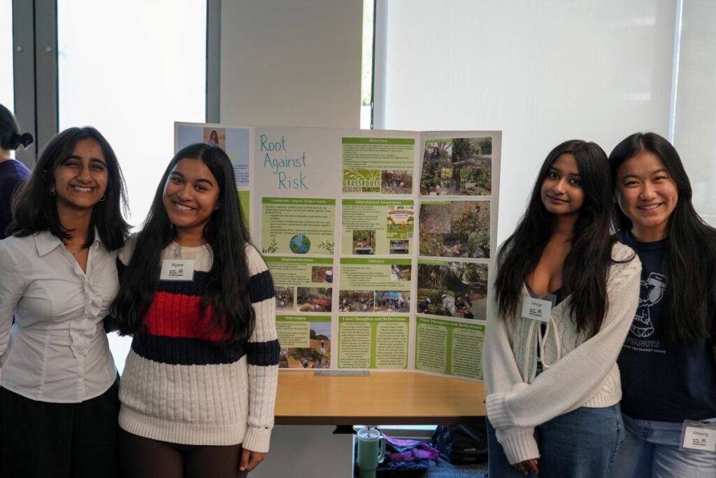 4 students posing in front of their "Root Against Risk" project poster