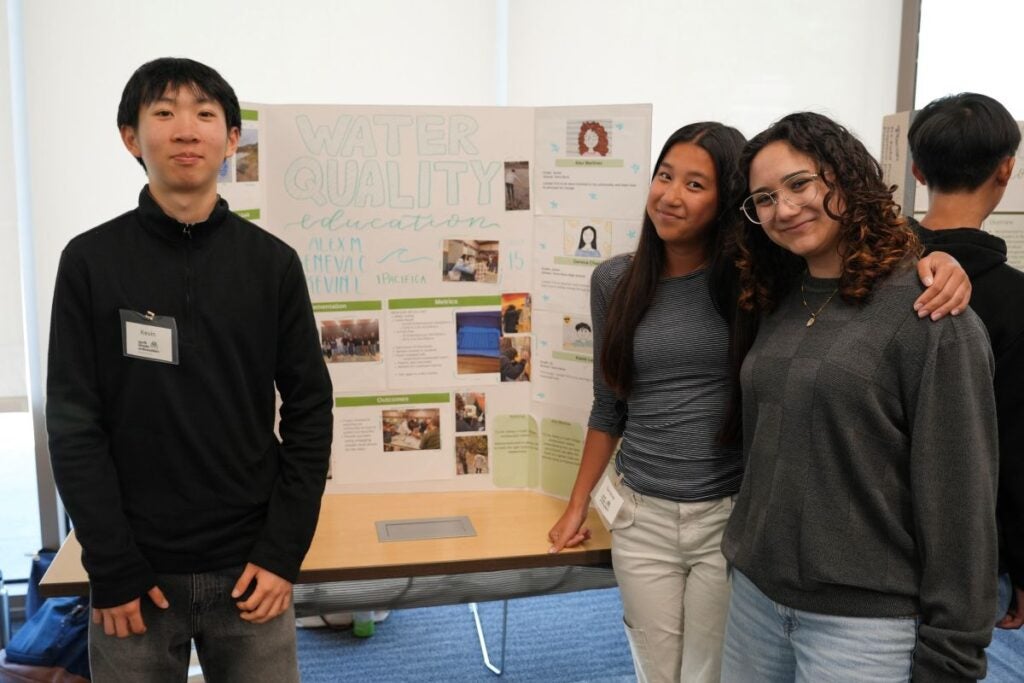 3 students posing in front of their "Water Quality Education" project poster